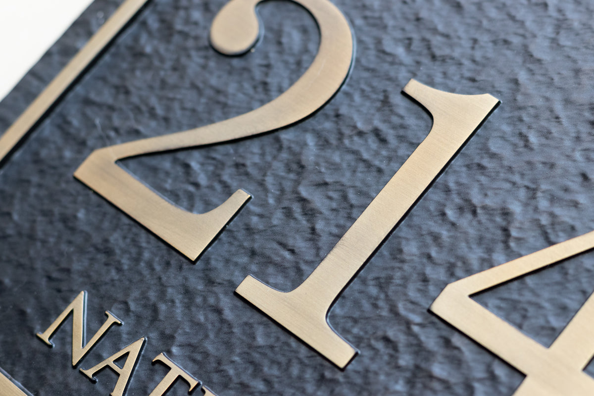 Close-up of antique brass house numbers on textured black aluminum plaque