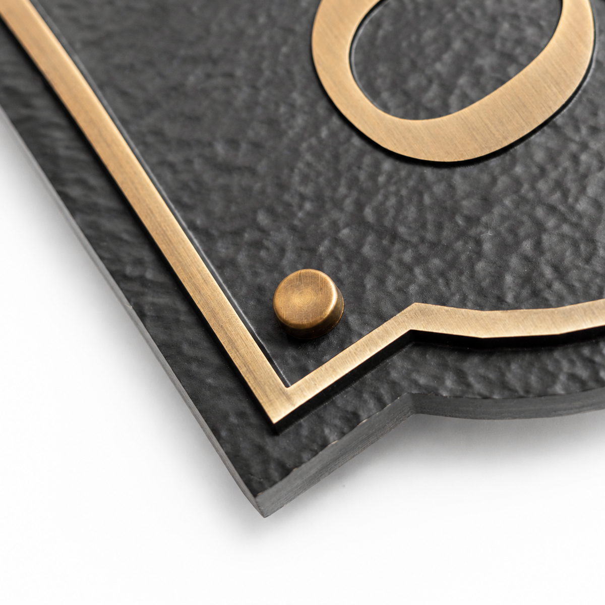 Close-up of textured black aluminum surface, brass border and raised wall mount