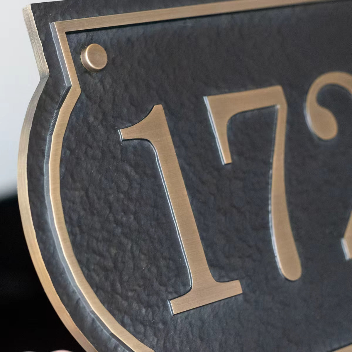 Close-up of antique brass house numbers on textured black solid aluminum